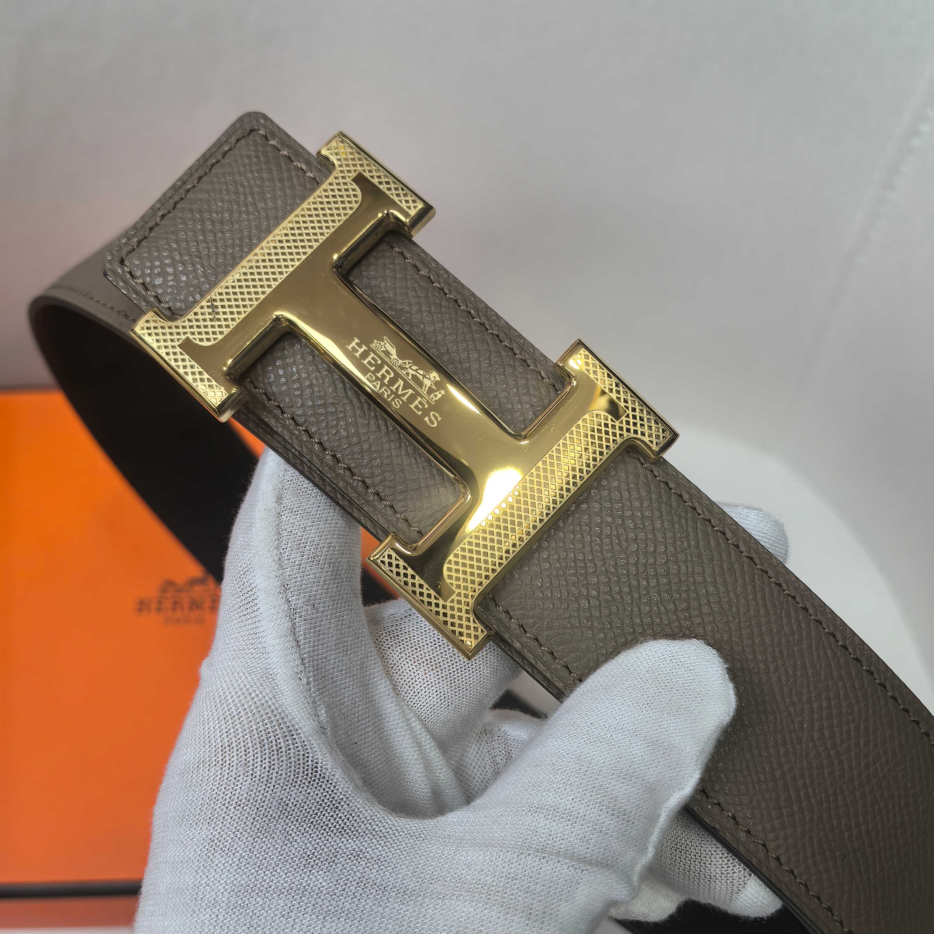 Taupe leather belt with gold H buckle, close-up of engraved buckle plate