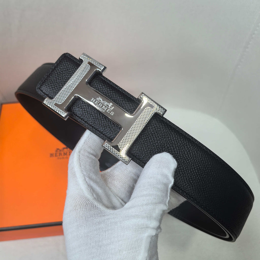 Black leather belt with silver buckle and wide strap end, shown with glove
