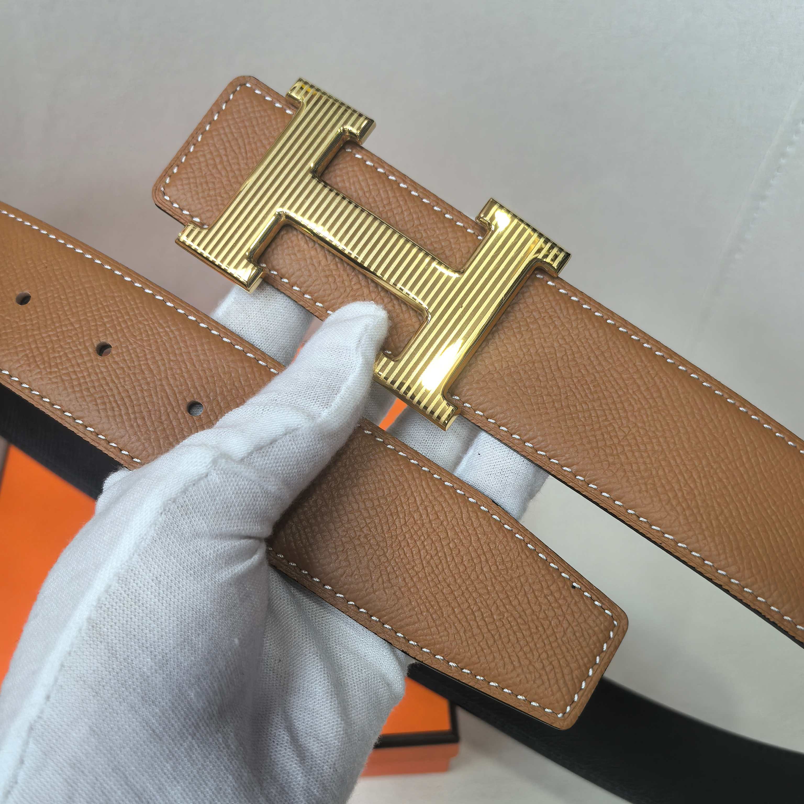 Brown leather belt buckle close-up with gold H design and stitched strap