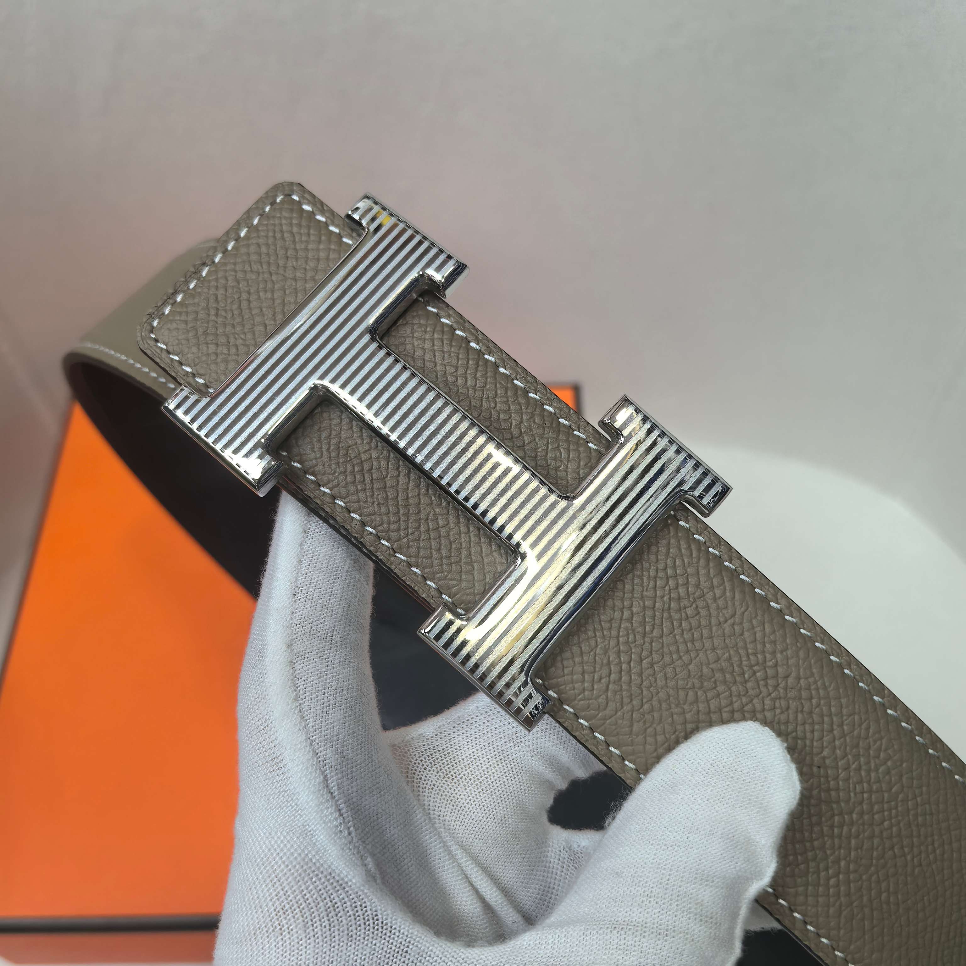 Leather belt with silver H buckle, taupe strap held in gloved hand