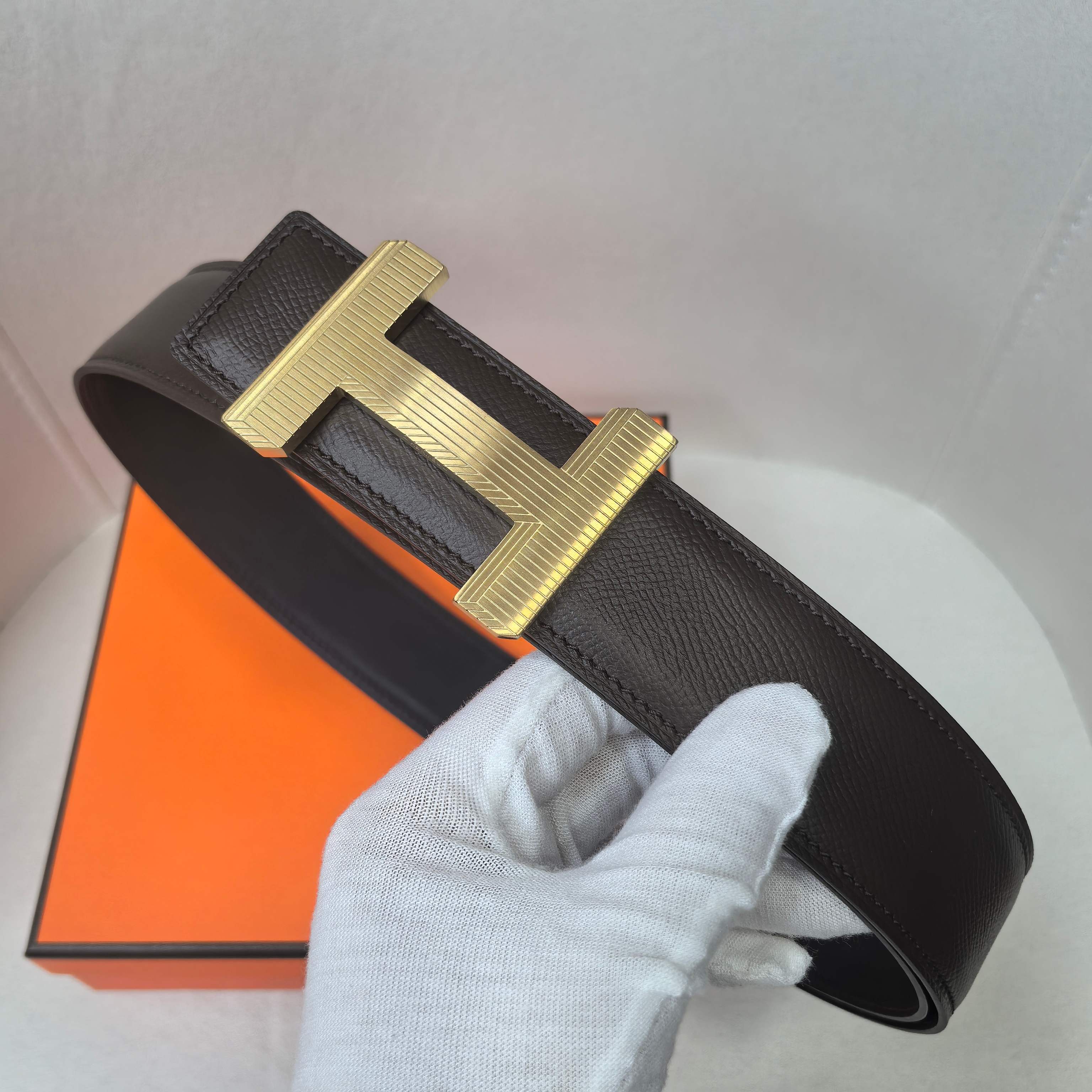 Black leather belt with gold-tone H buckle, curved strap end and stitching.