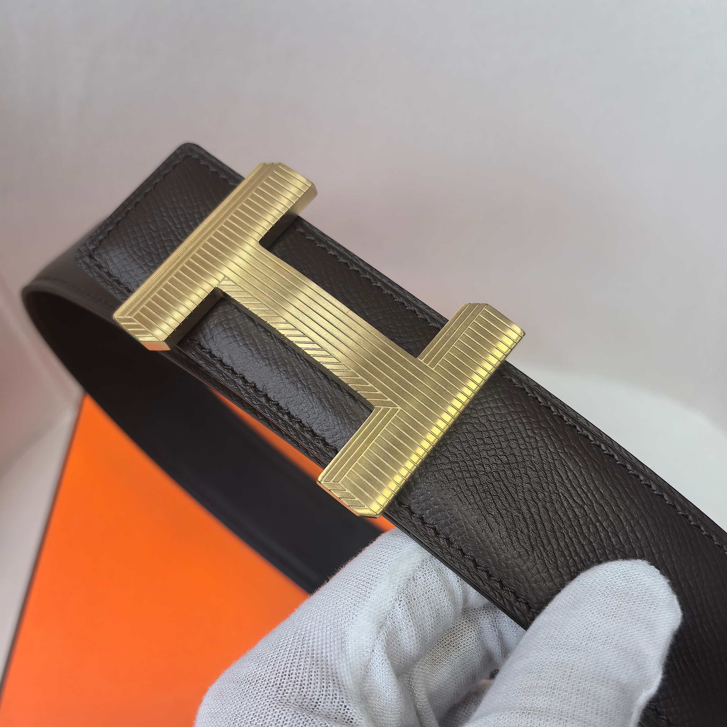 Black leather belt with gold-tone H buckle, textured leather strap and keeper.
