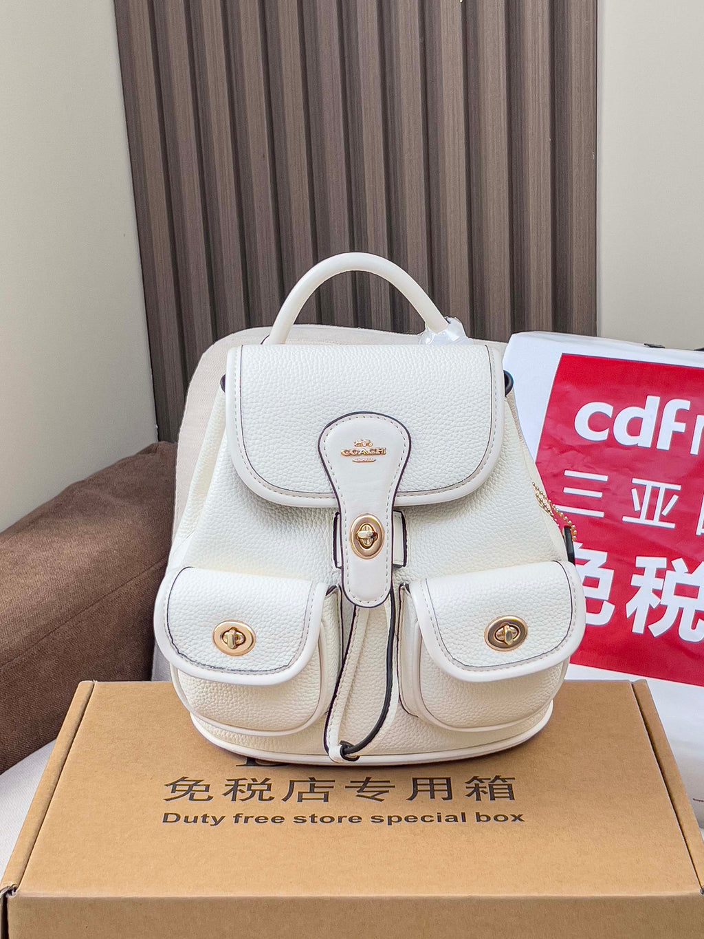 White mini backpack bag with top handle, front flap, and gold buckles
