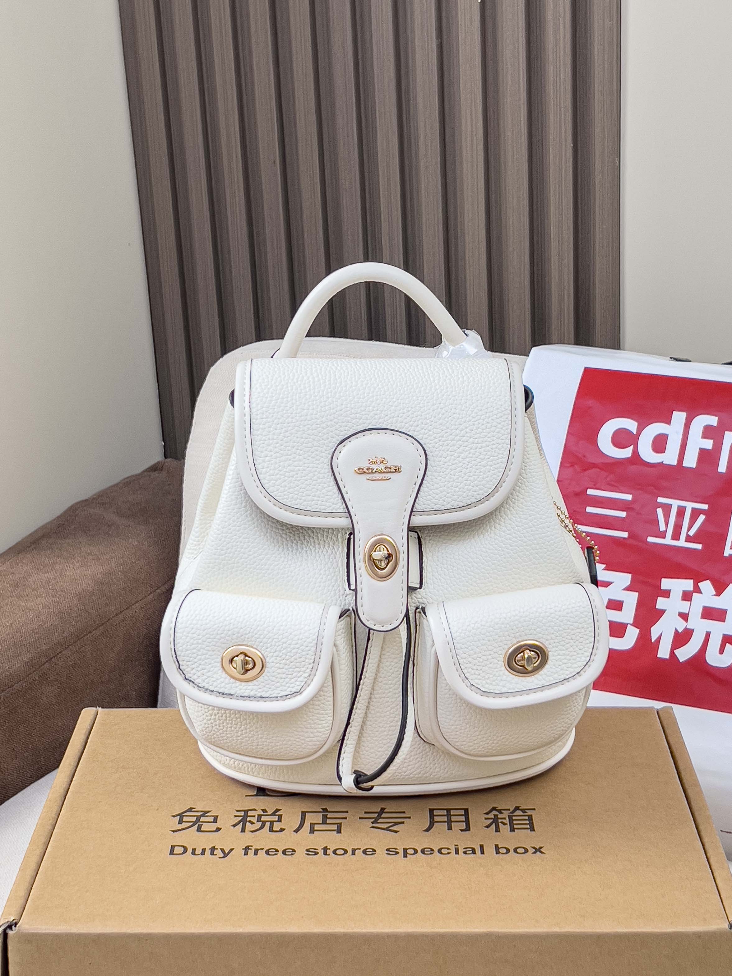White mini backpack bag with top handle, front flap, and gold buckles