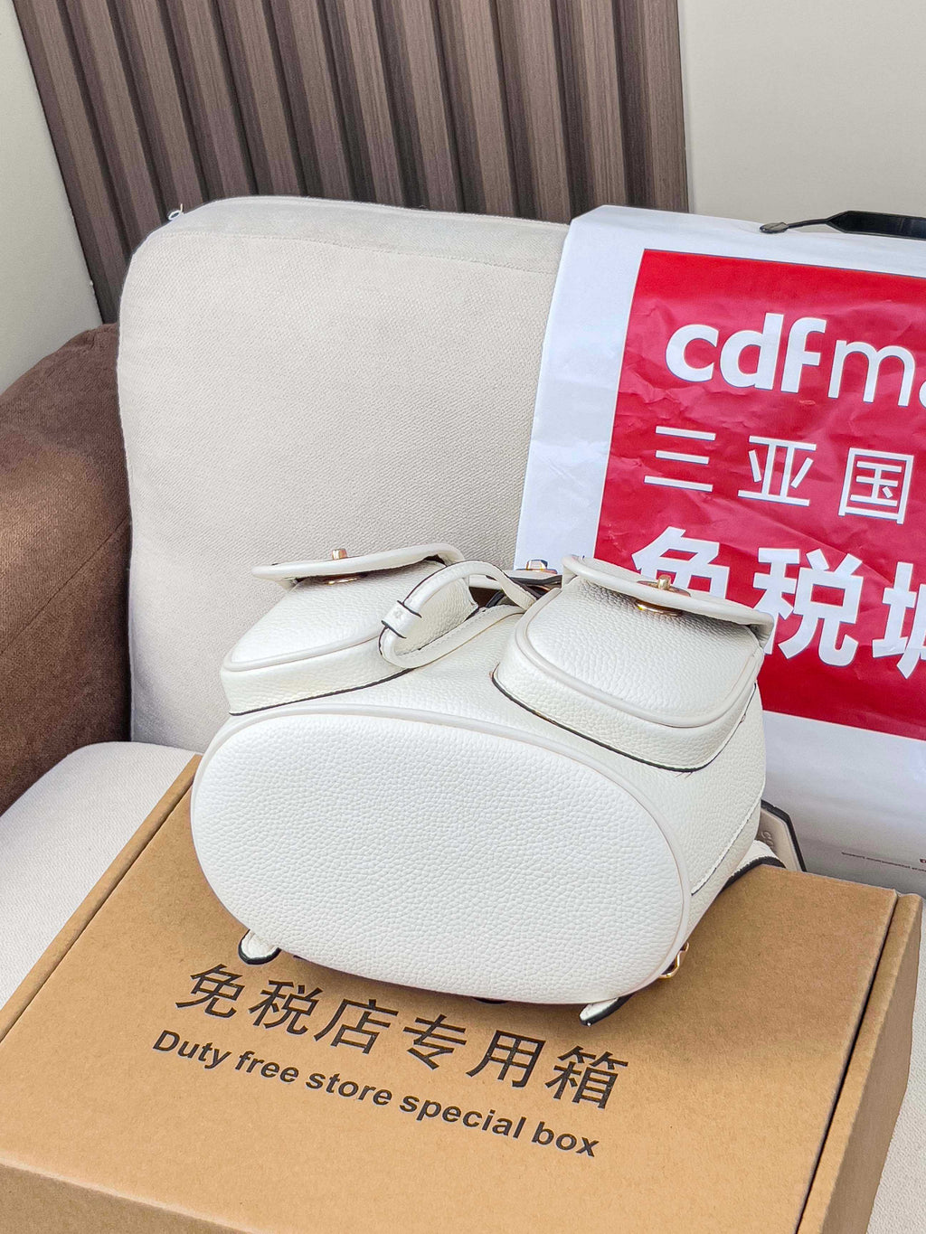White mini backpack bag with front flap, gold hardware, and side pocket
