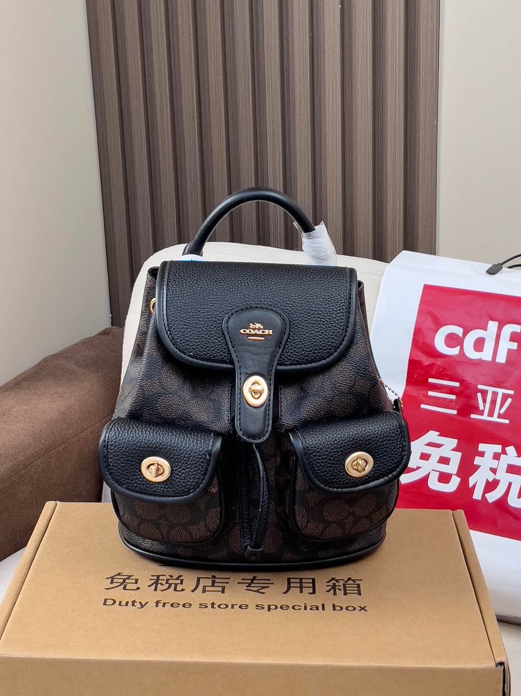 Coah mini backpack with black top flap and dual front pockets, gold button details