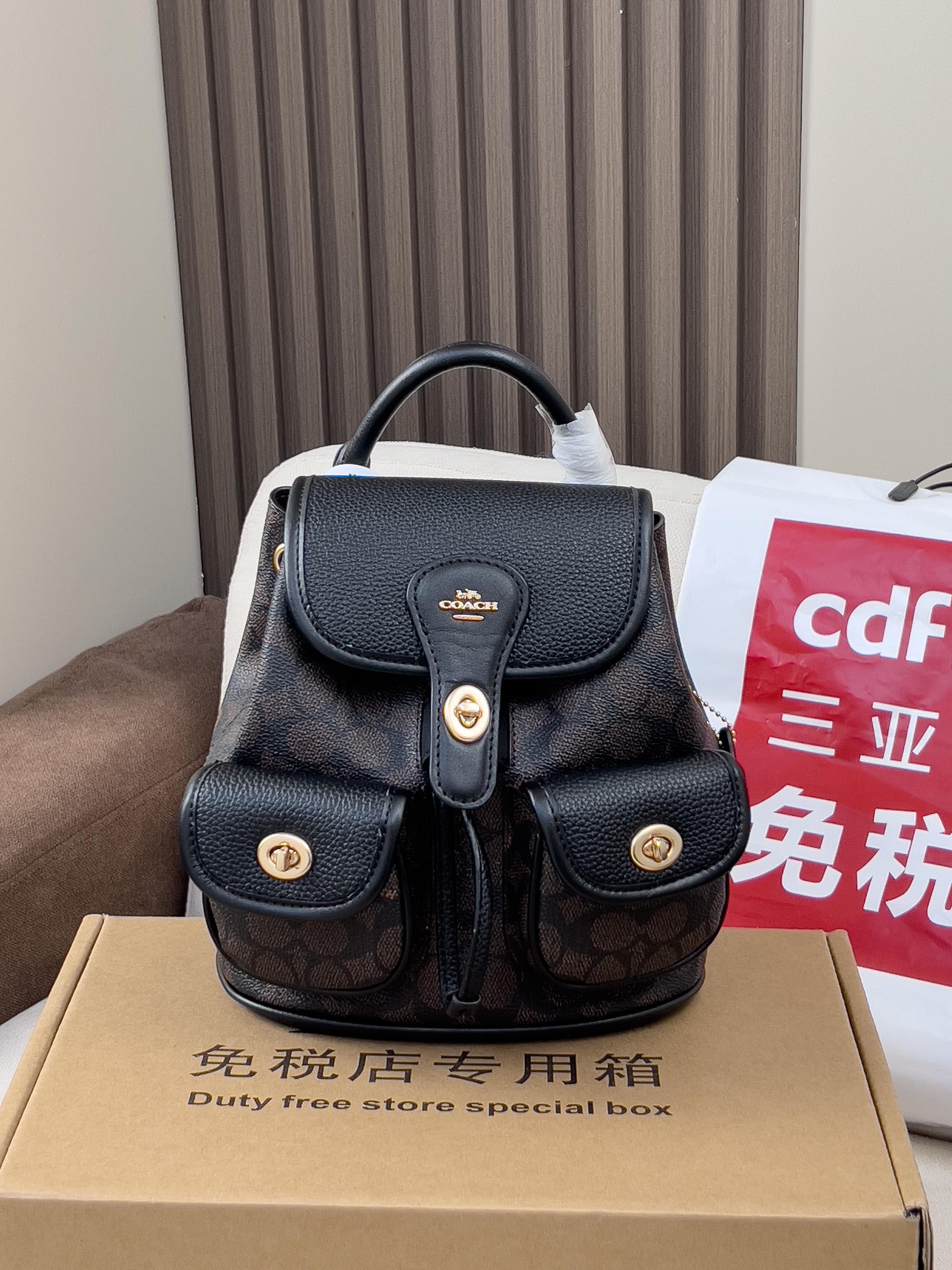 Coah mini backpack with black top flap and dual front pockets, gold button details