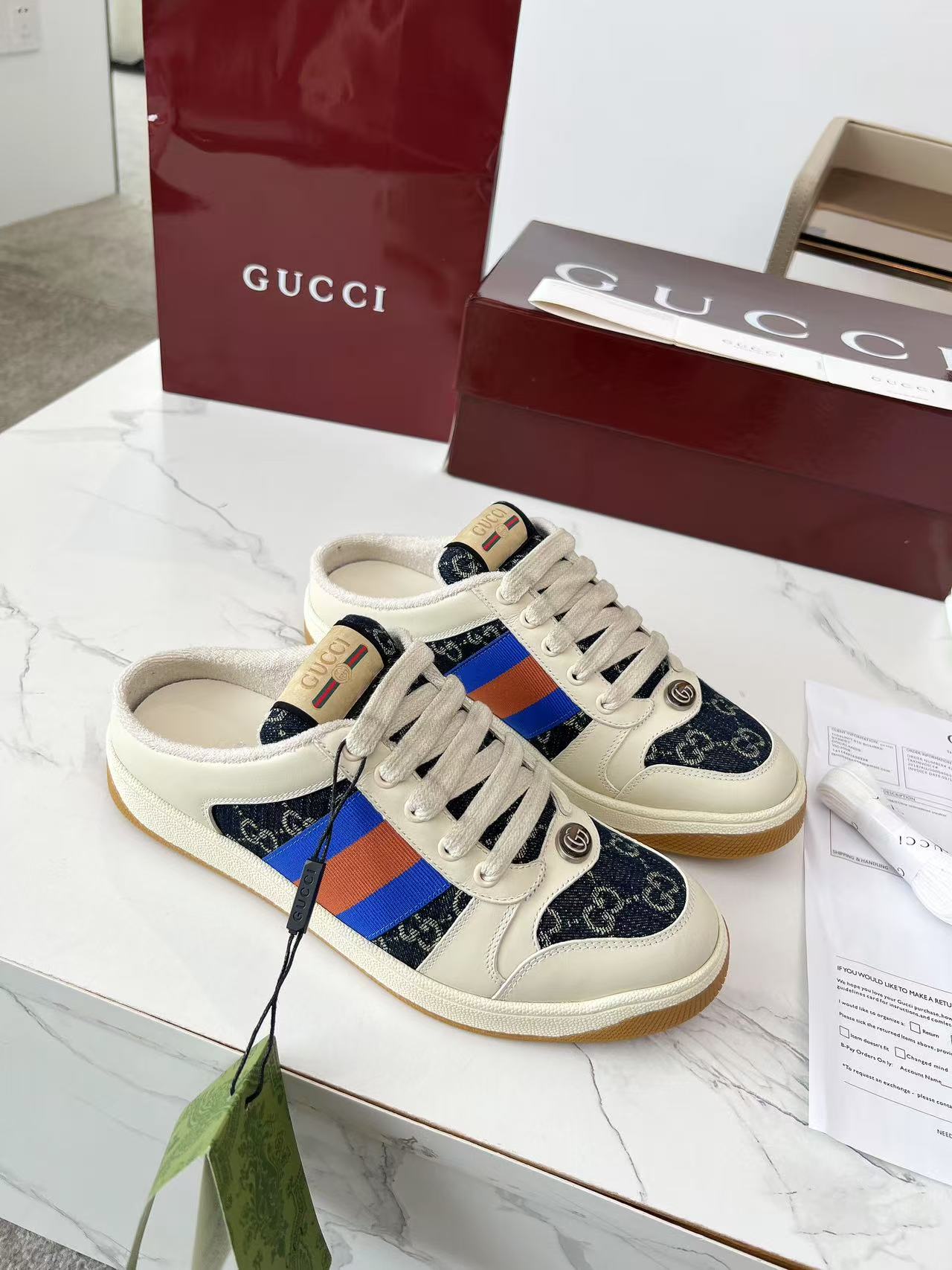 Gucci low-top sneakers with cream base, navy GG canvas, and blue-orange stripe accents