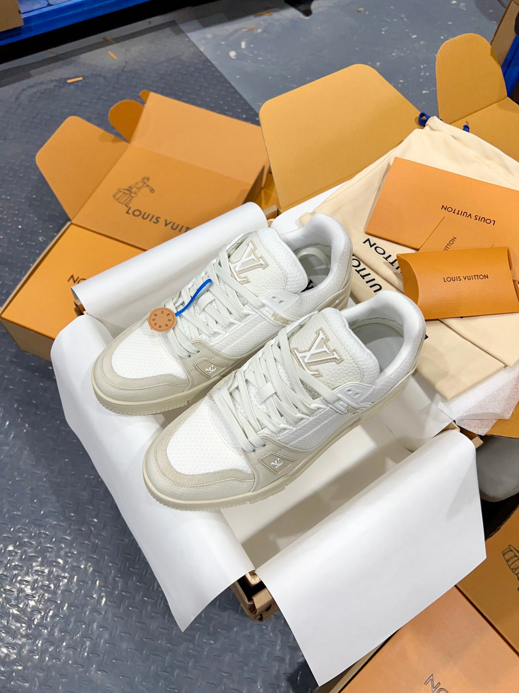 White Louis Vuitton trainer shoes on display box, showing laces and side LV emblem.