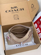 Coah hobo bag shown open in box, light beige monogram, top zip and leather handle strap