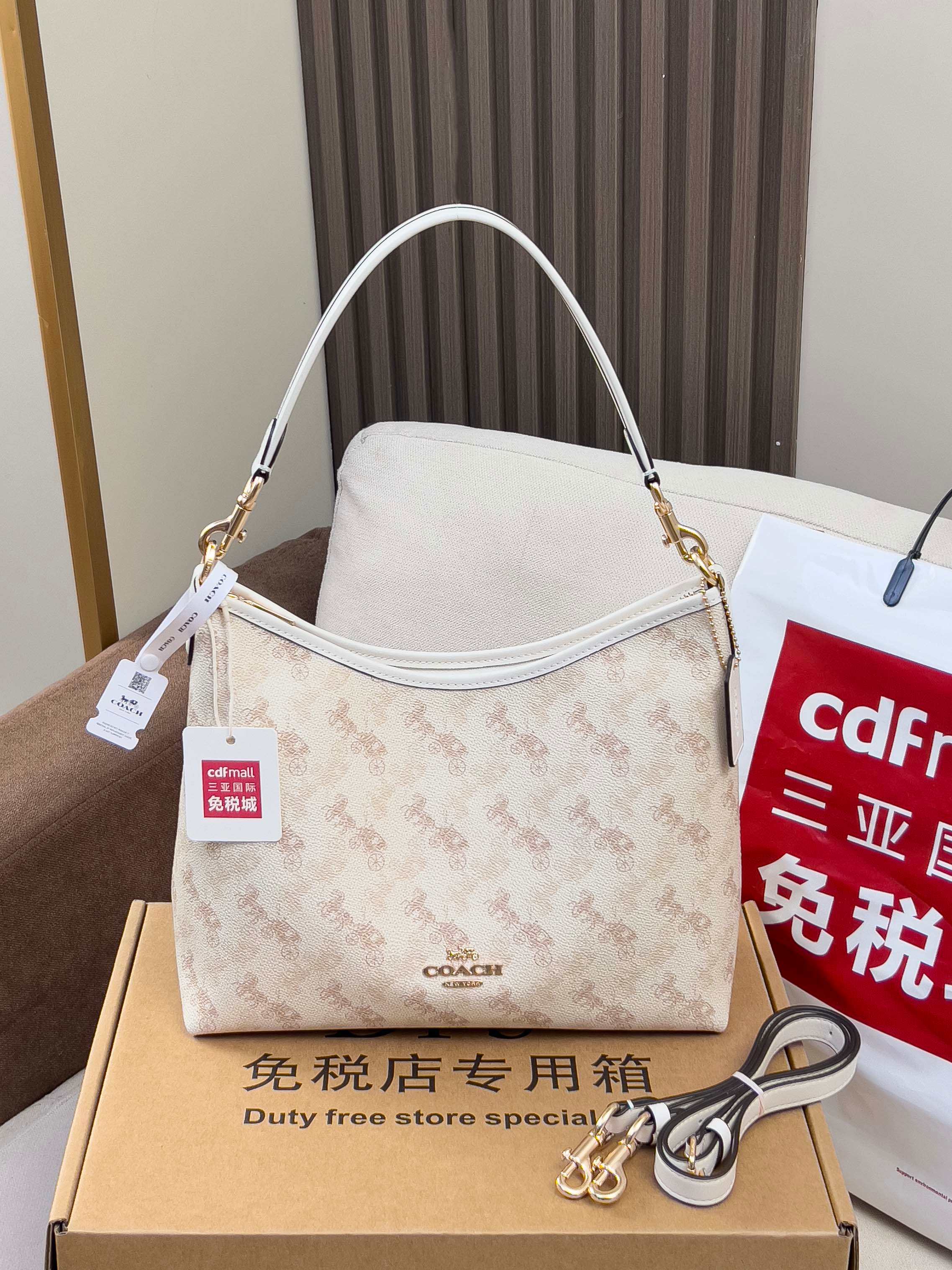 Light beige patterned shoulder bag with white top handle and gold hardware, in box packaging