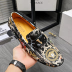 Printed slip-on loafers held in hand; black upper with gold motif and orange lining