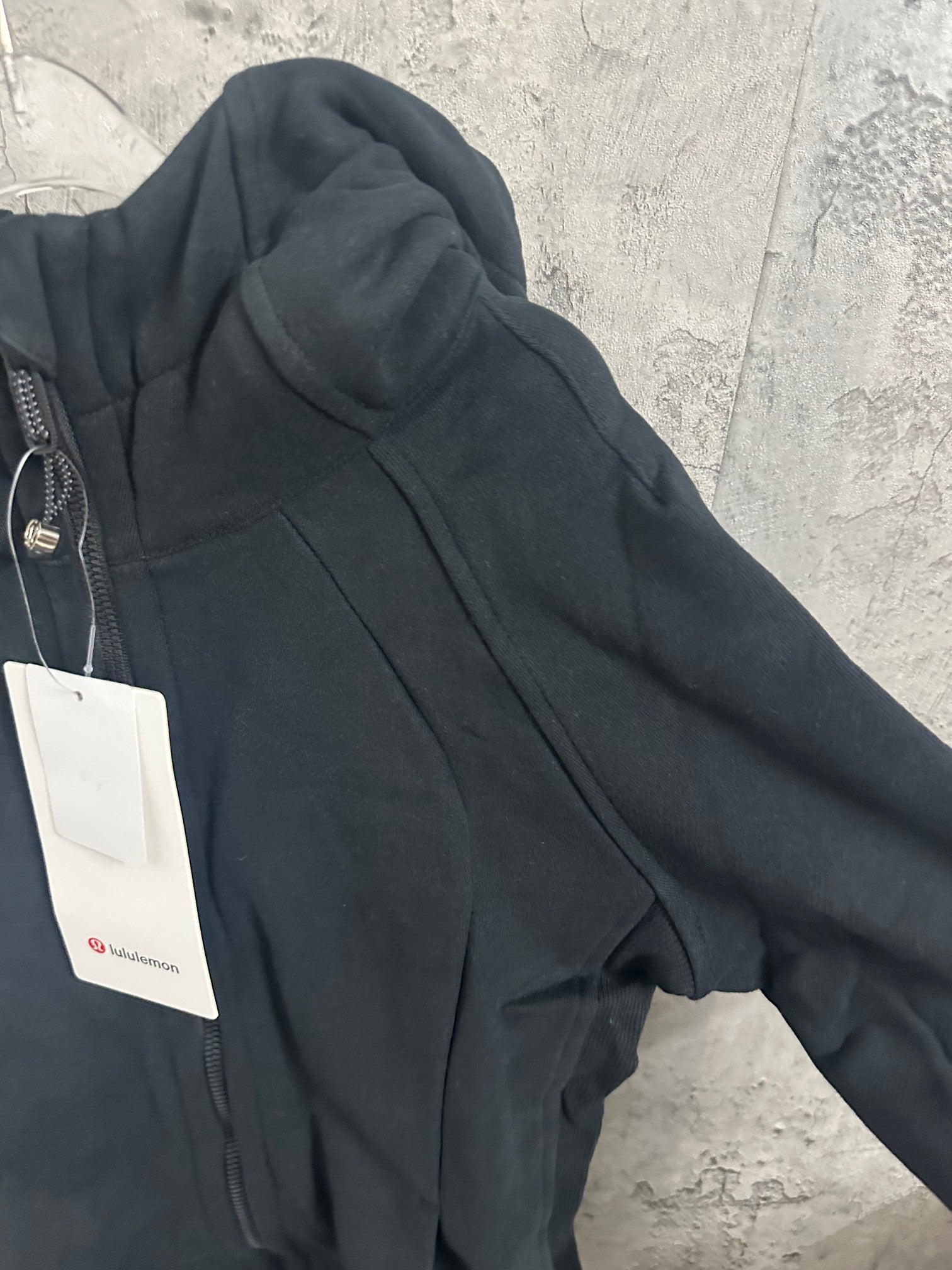 Dark zip-up hooded jacket side view with front zipper and hood detail, hanging tag