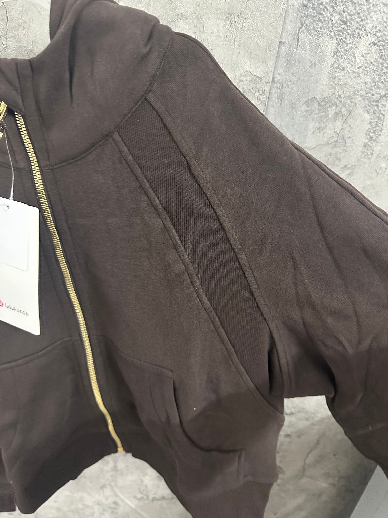 Dark zip-up hoodie sleeve with ribbed cuff and gold-trimmed zipper