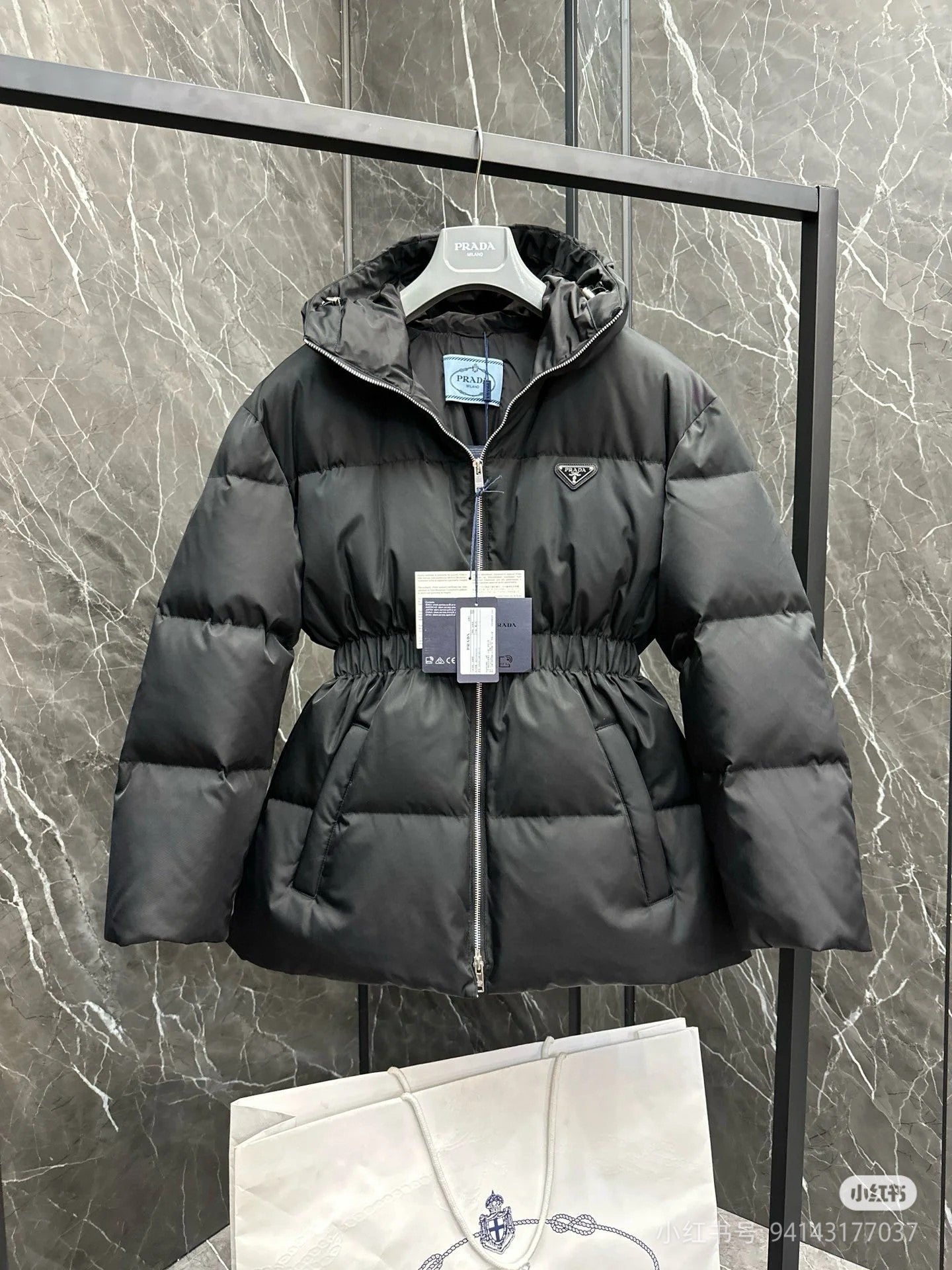 Black hooded puffer jacket with front zipper and cinched waist detail