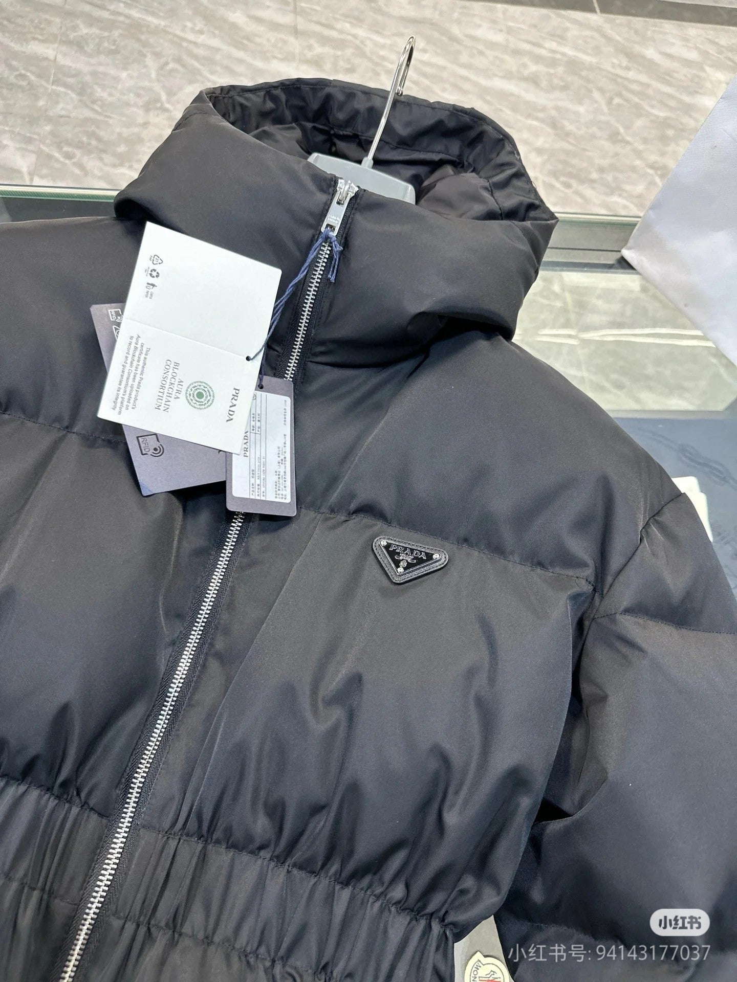 Black hooded puffer jacket close-up with front zipper and logo patch