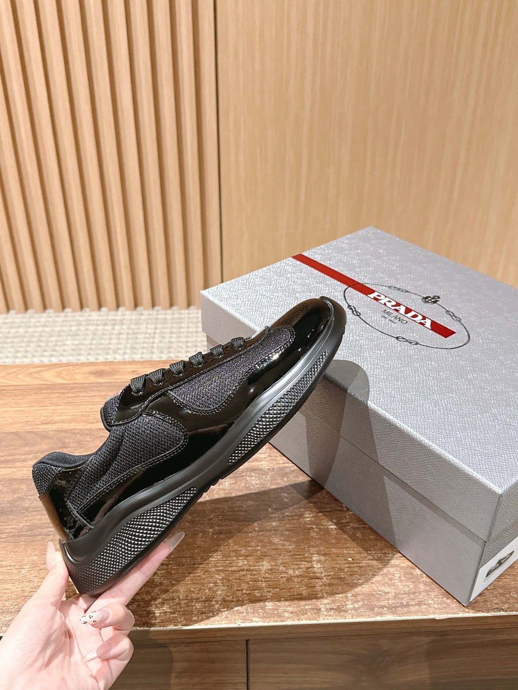 Black lace-up sneaker held in hand beside gray gift box with red logo