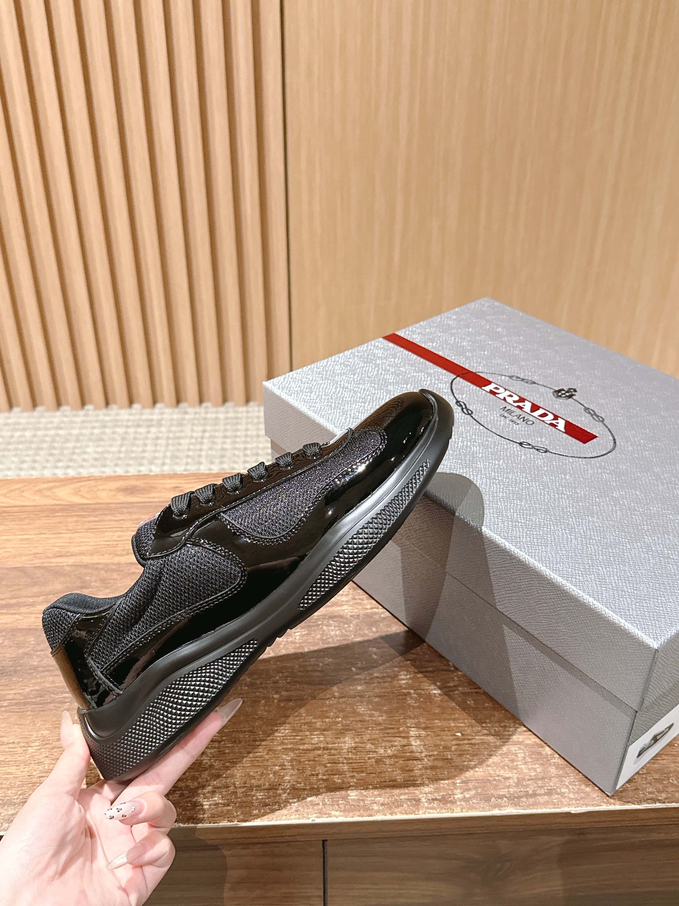 Black lace-up sneaker held in hand beside gray gift box with red logo
