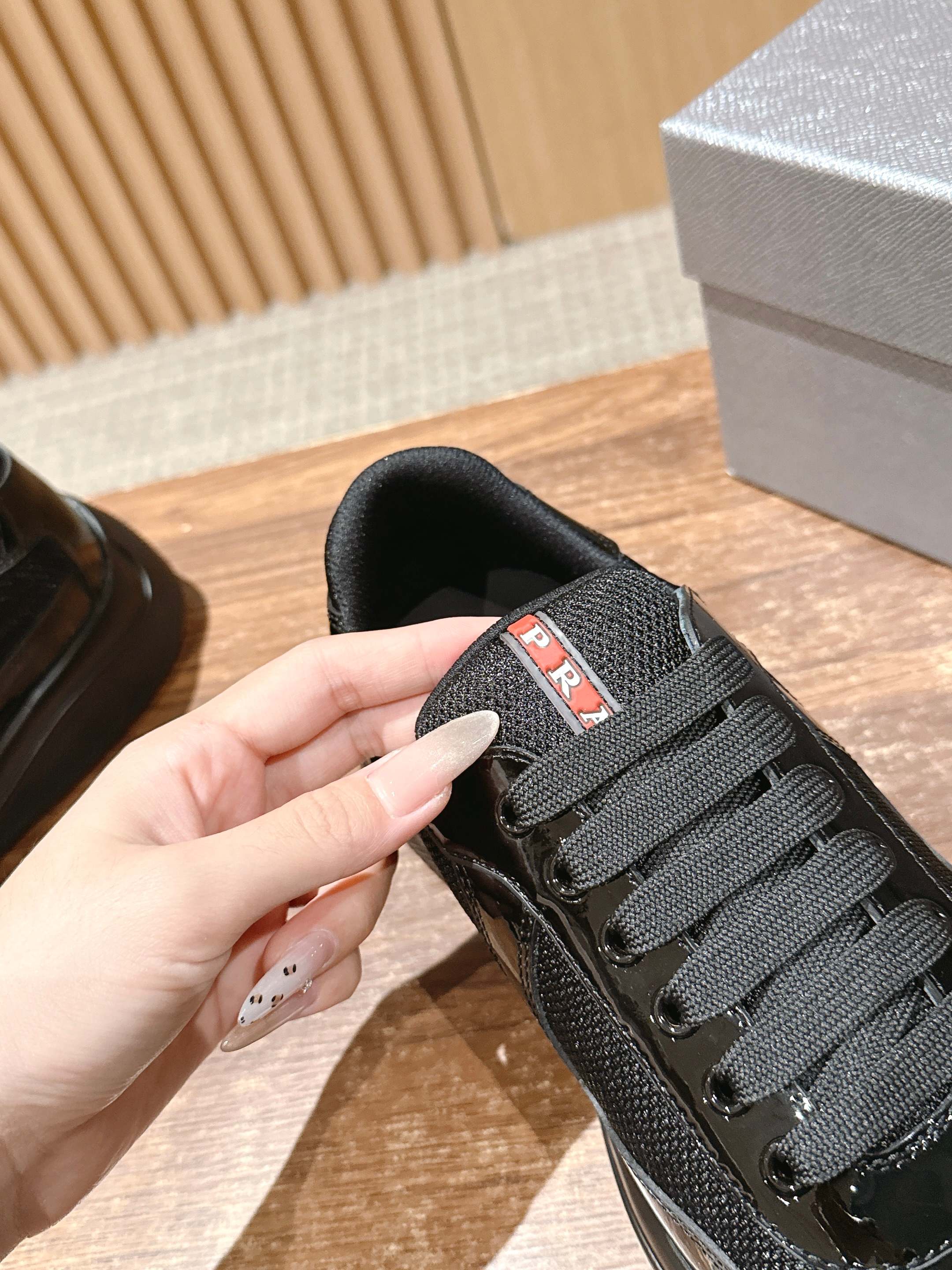 Black sneaker tongue with red and white logo patch, lace-up detail