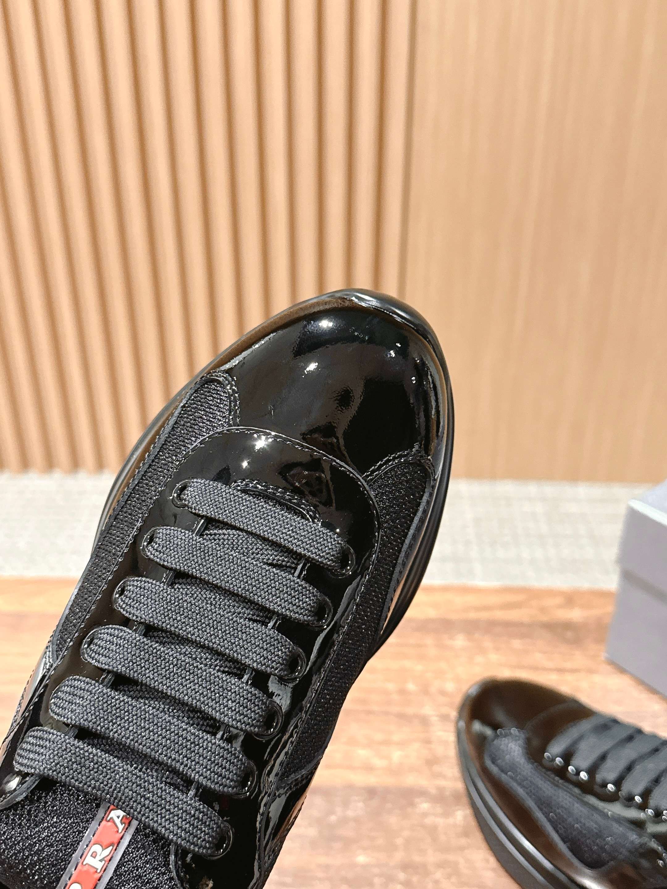 Black sneaker front with textured fabric and glossy patent toe cap, lace-up