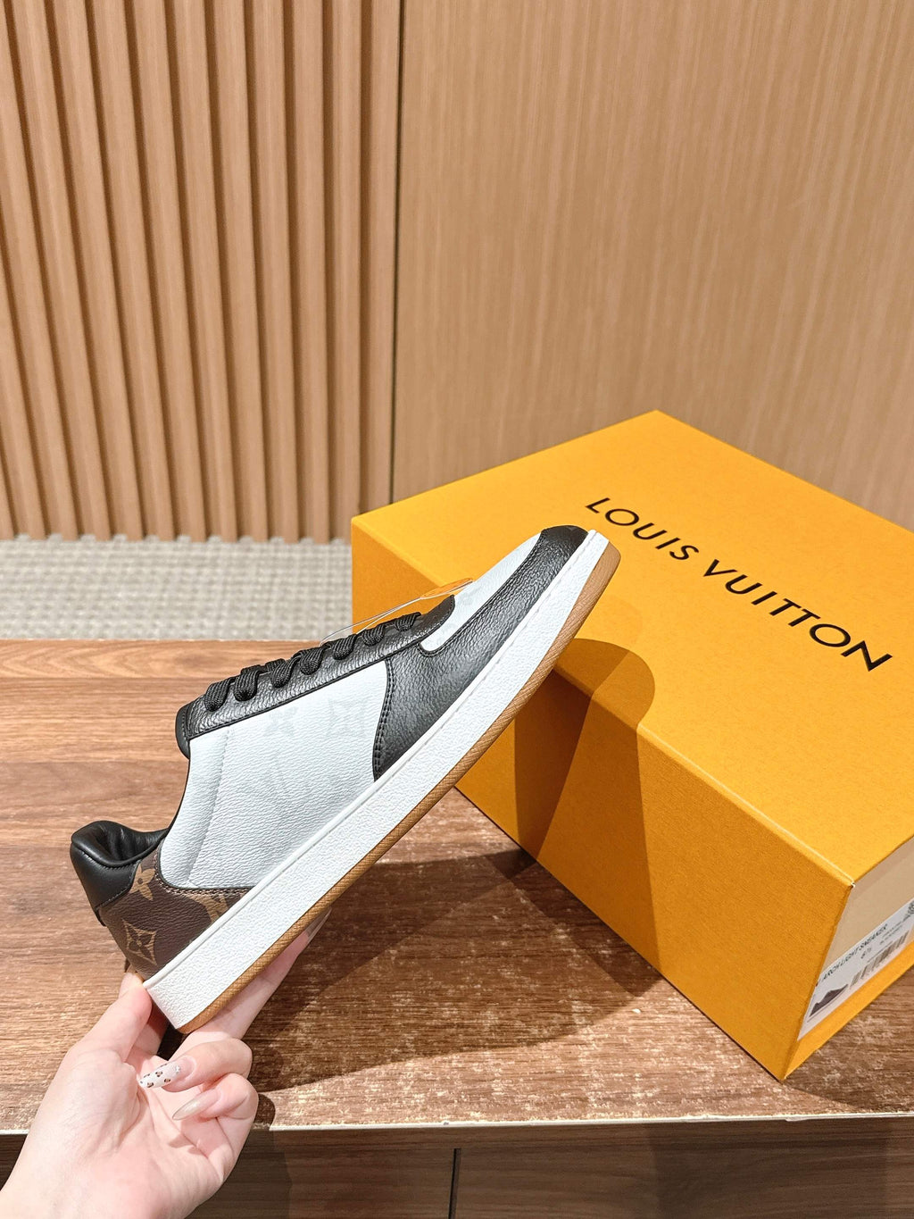 Low-top Louis Vuitton sneakers, black and white with textured monogram, held in hand