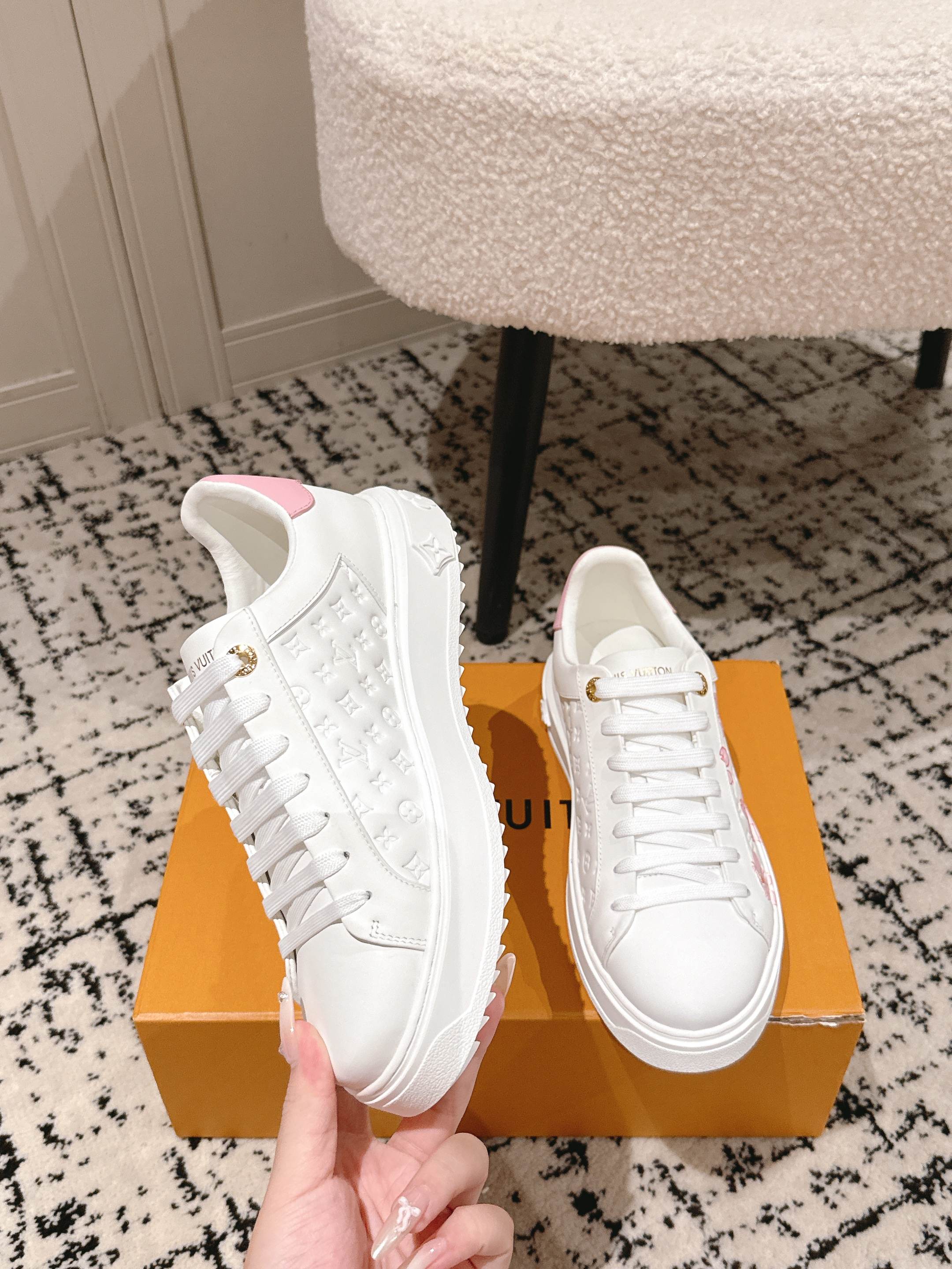 Louis Vuitton white sneakers, front view, with white laces and subtle pink floral detail