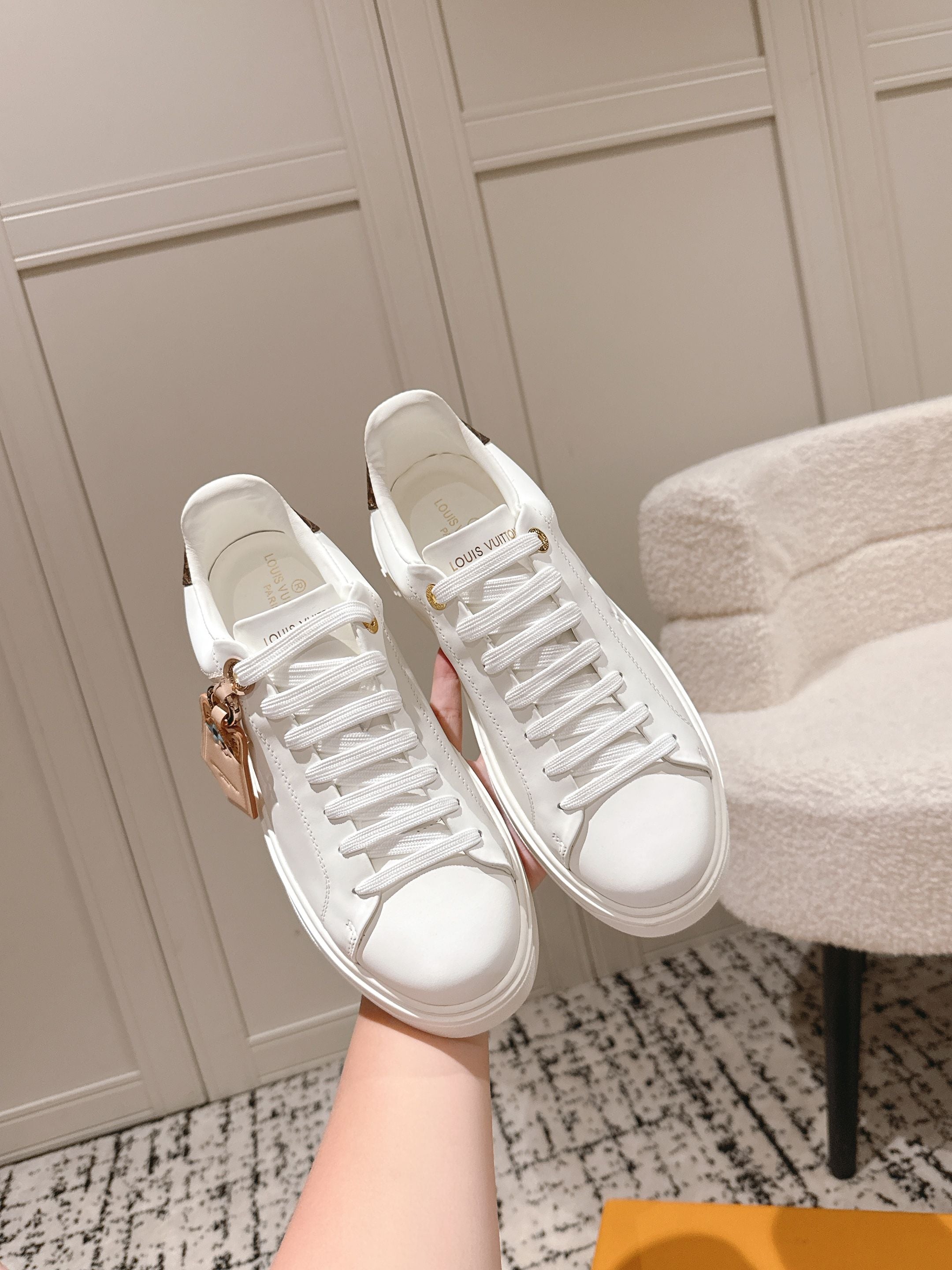 White low-top sneakers with white laces and gold-tone hardware detail