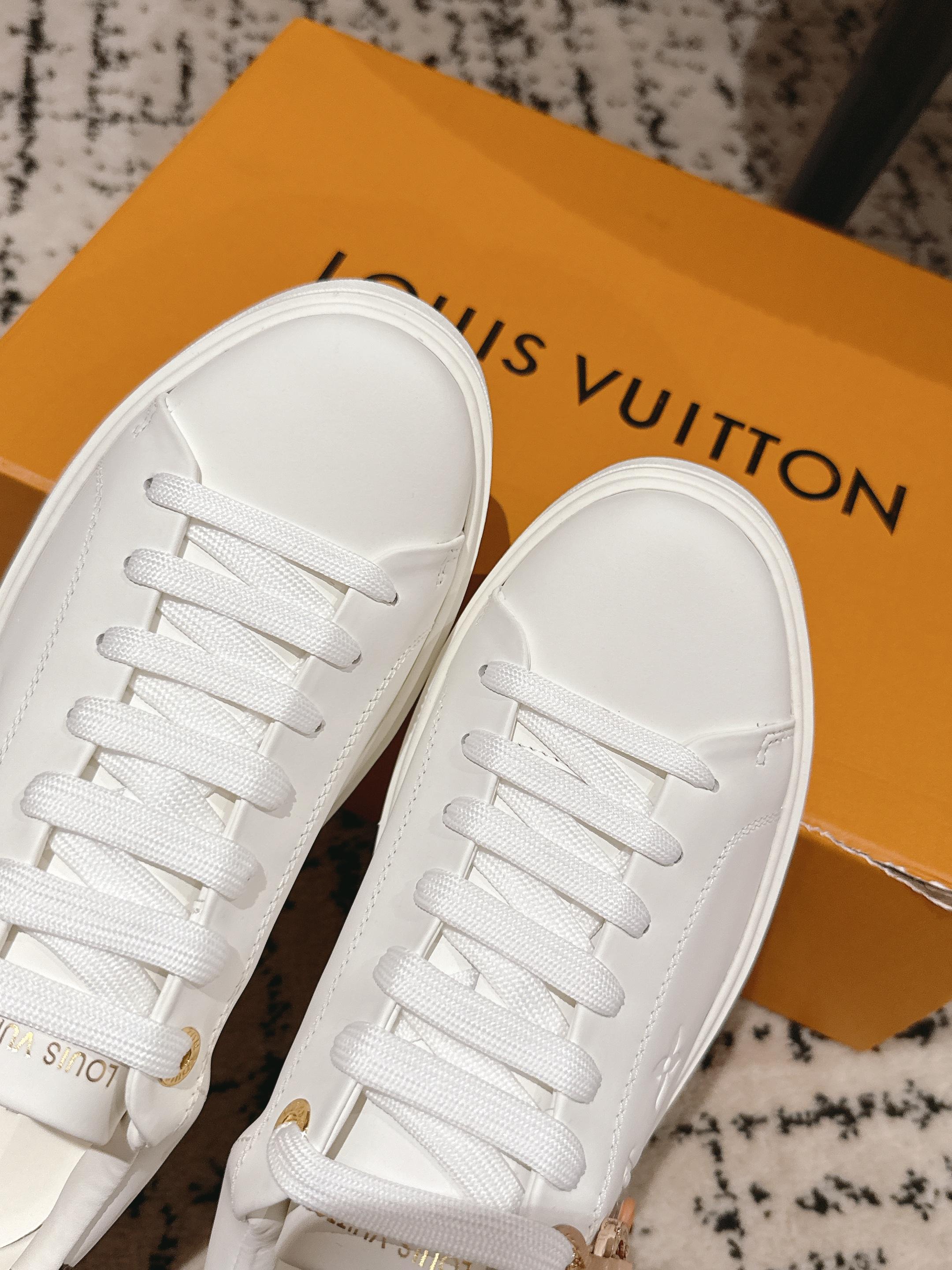 Close-up of white lace-up sneakers with matching tongues and gold logo trim