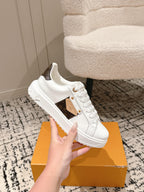 White lace-up low-top sneaker with dark-brown logo patch, placed on orange box