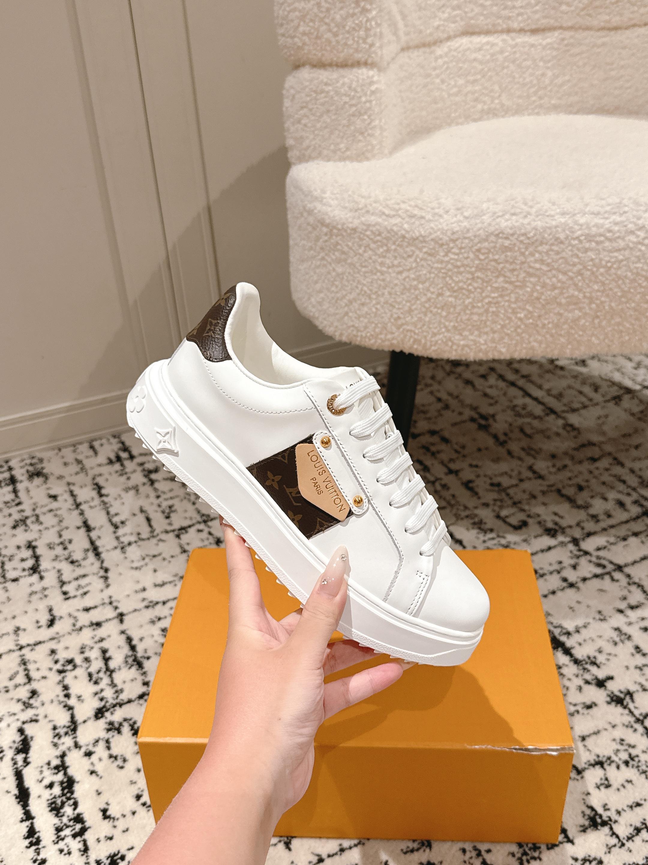 White lace-up low-top sneaker with dark-brown logo patch, placed on orange box