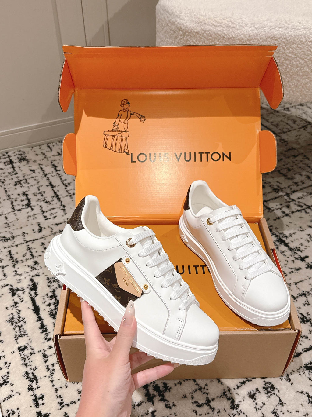 White Louis Vuitton low-top sneakers with dark-brown logo patch, shown in orange box