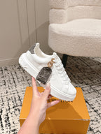 White low-top sneakers with dark check-pattern strap detail and gold lace eyelets