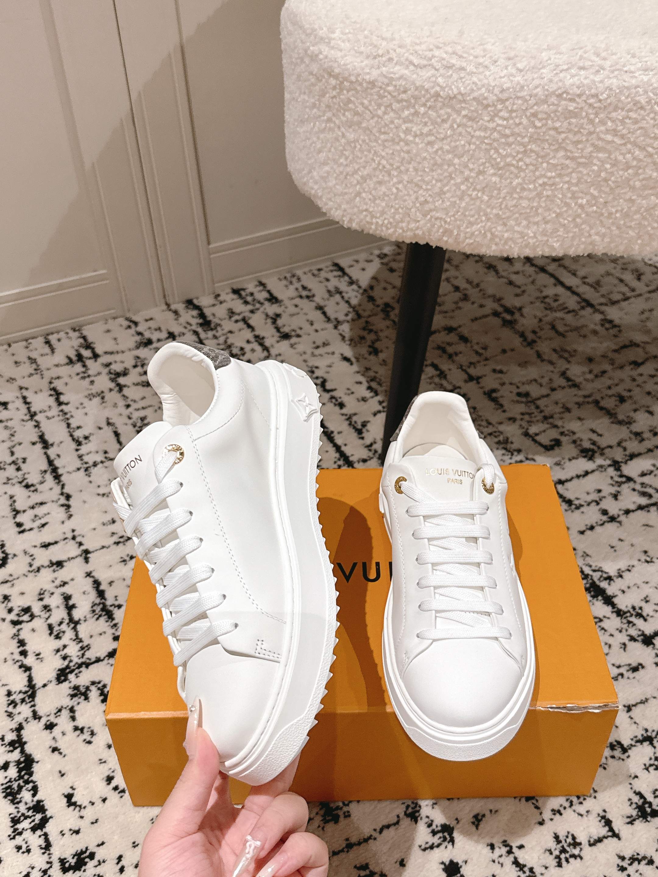 White low-top sneakers on orange box, lace-up design with gold logo detail