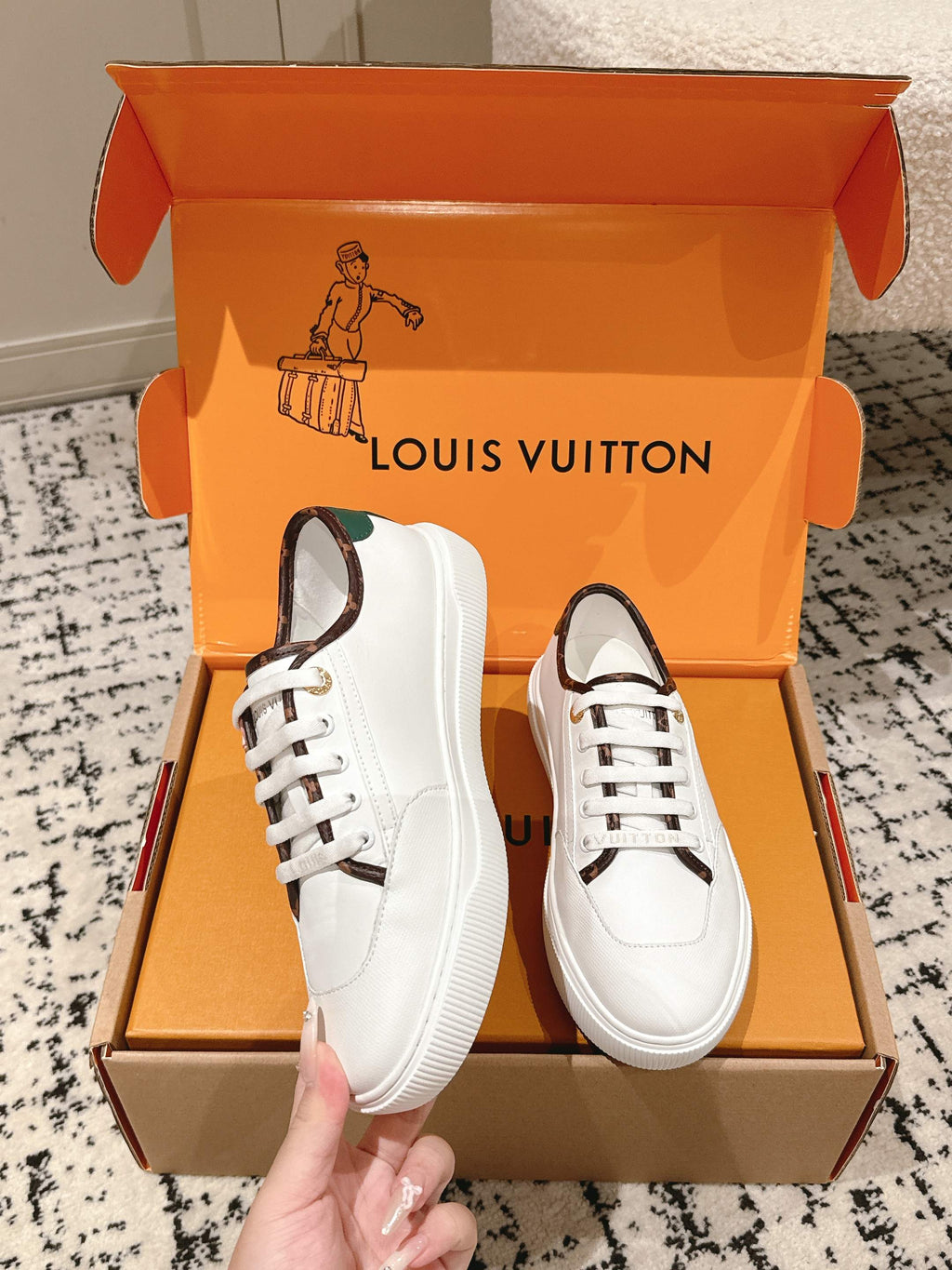 White leather lace-up sneakers on orange gift box, gold lace eyelets