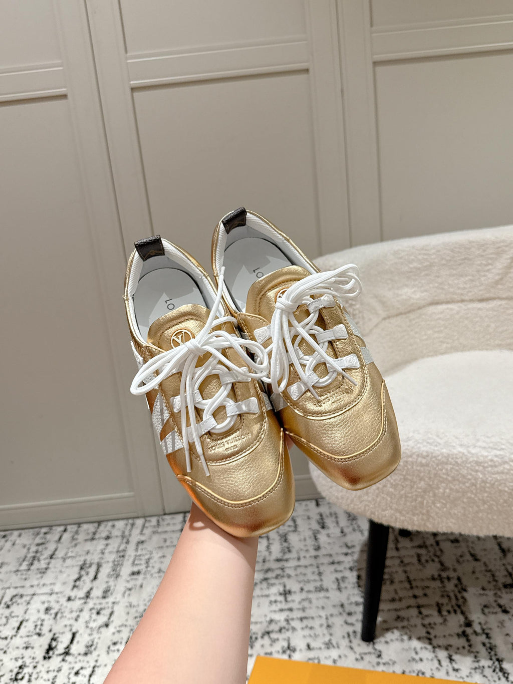 Gold and white leather sneakers with white laces, held up in front of shoebox.