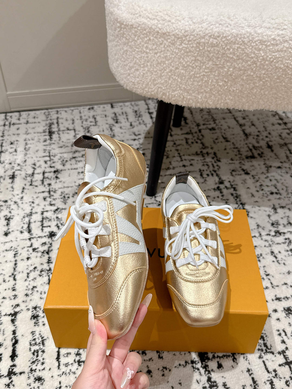Gold and white low-top leather sneakers with white laces, side view by shoebox.
