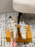 Gold and white low-top leather sneakers with white laces, side view by shoebox.