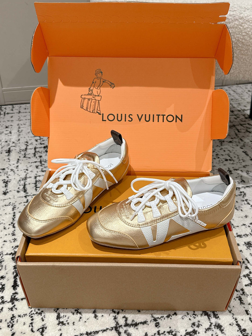 Gold and white leather sneakers with white laces, placed on open shoebox.