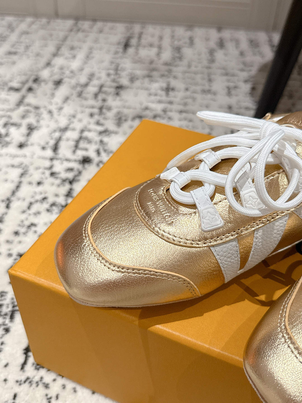 Gold leather sneaker with white laces and white paneling, close-up on shoebox.