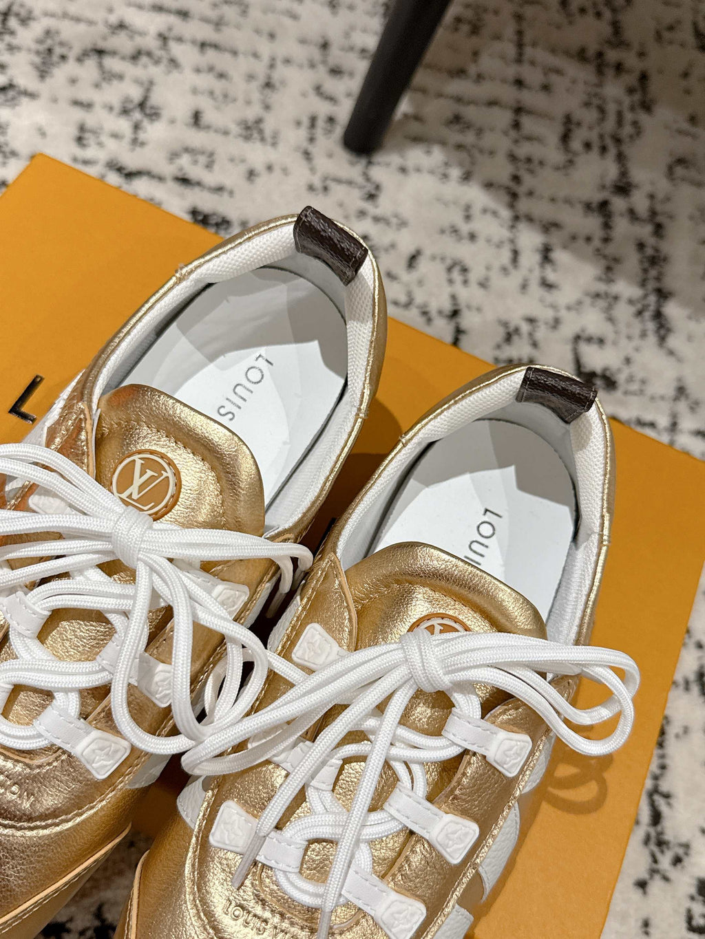 Gold leather sneakers with white laces, close-up of toe and tongue on shoebox.