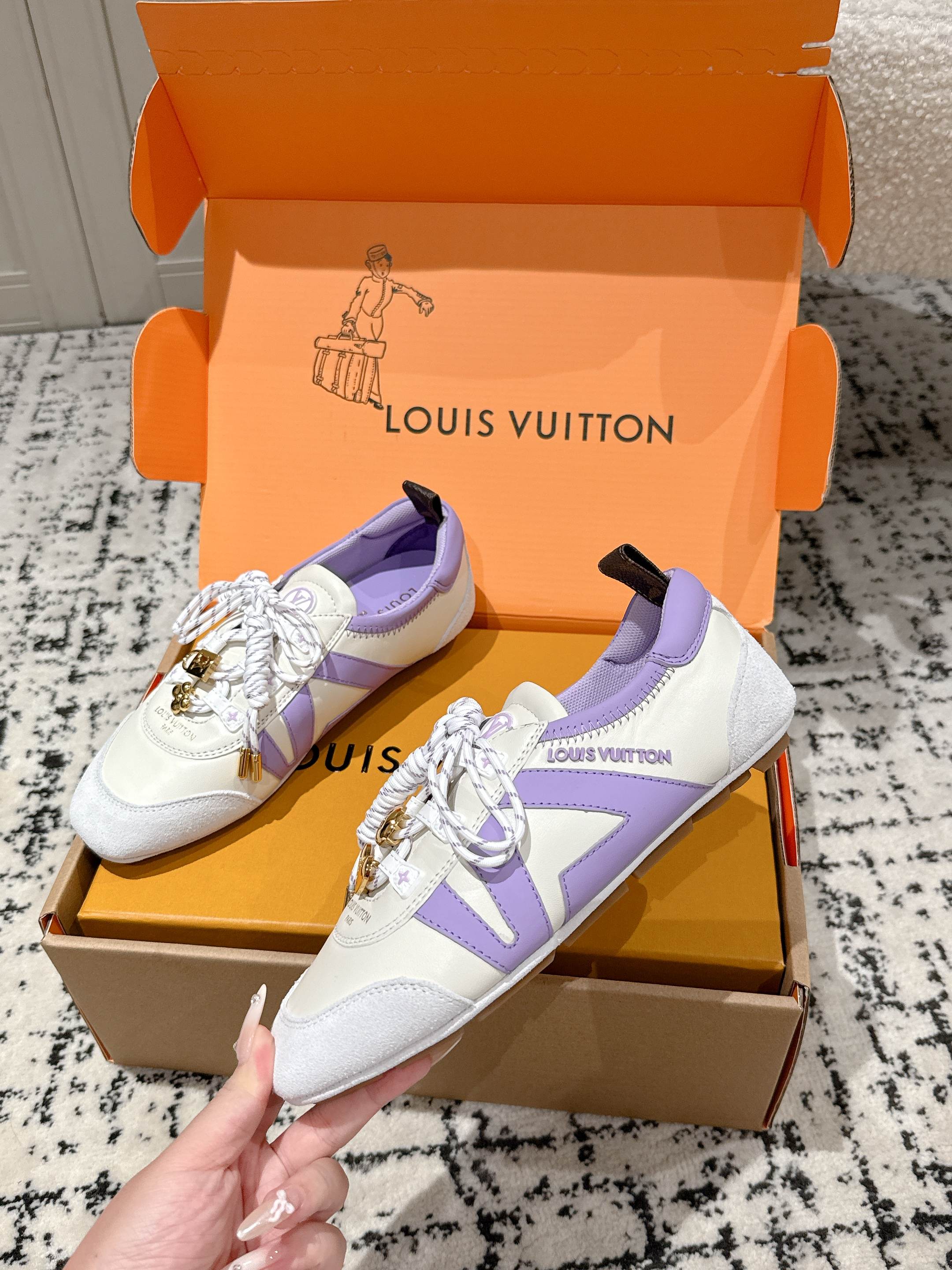 White and lavender Louis Vuitton lace-up sneakers with gold charm hardware on open box