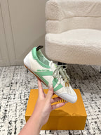 White low-top sneakers with mint green trim and lace ties, held above box