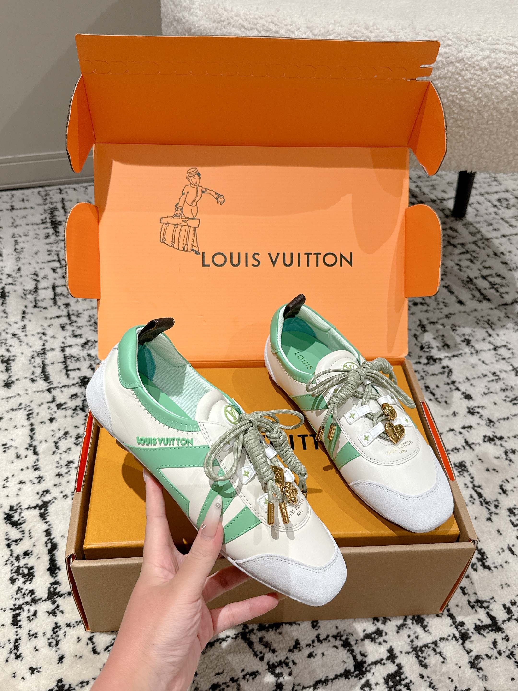 White and mint lace-up sneakers with gold charm, resting in Louis Vuitton shoebox