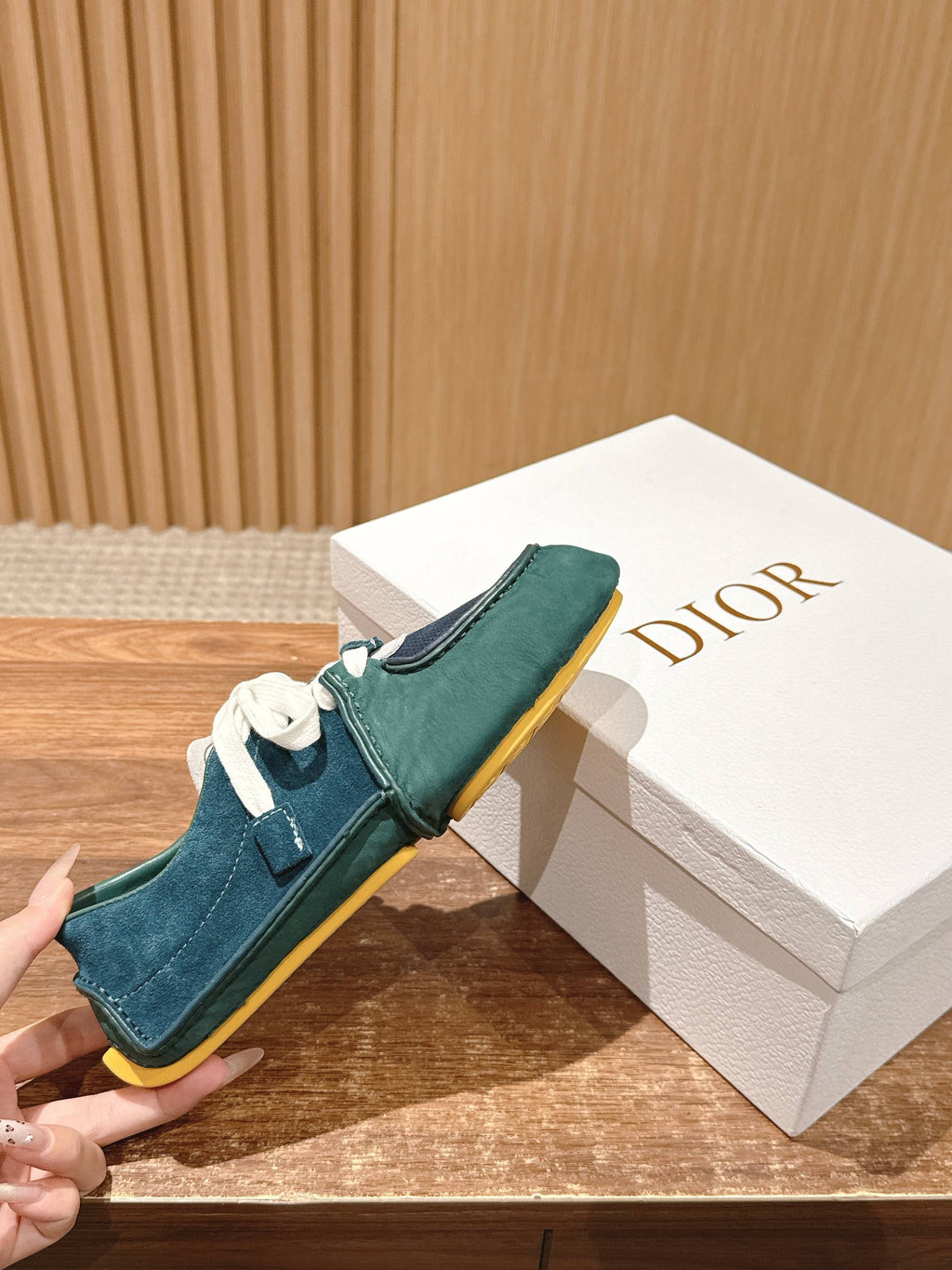 Teal and navy low-top sneakers held near a Dior logo box, yellow-edged sole