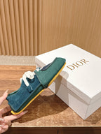 Teal and navy low-top sneakers held near a Dior logo box, yellow-edged sole