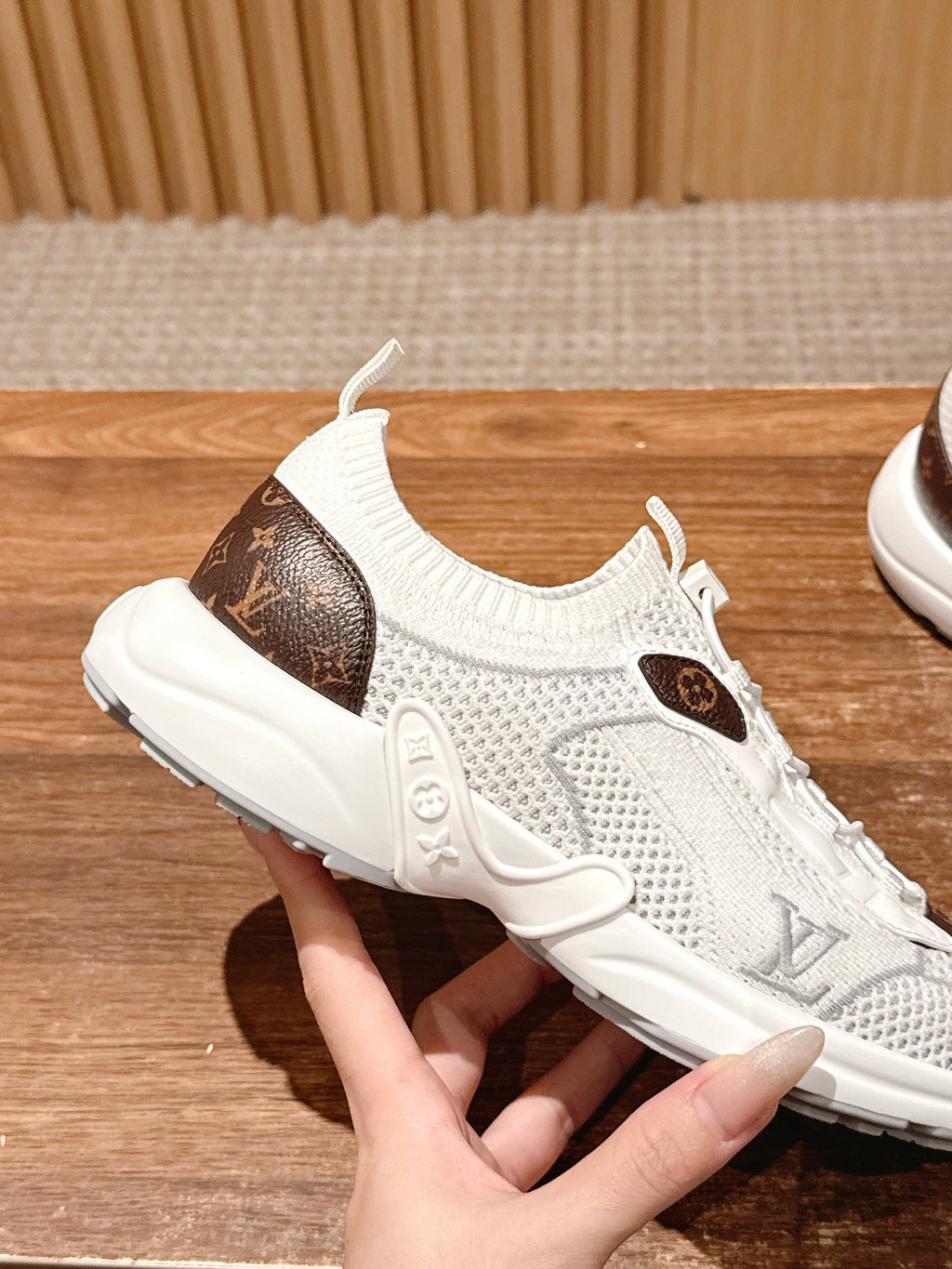 Louis Vuitton unisex white sneakers being held; brown logo patch on mesh upper