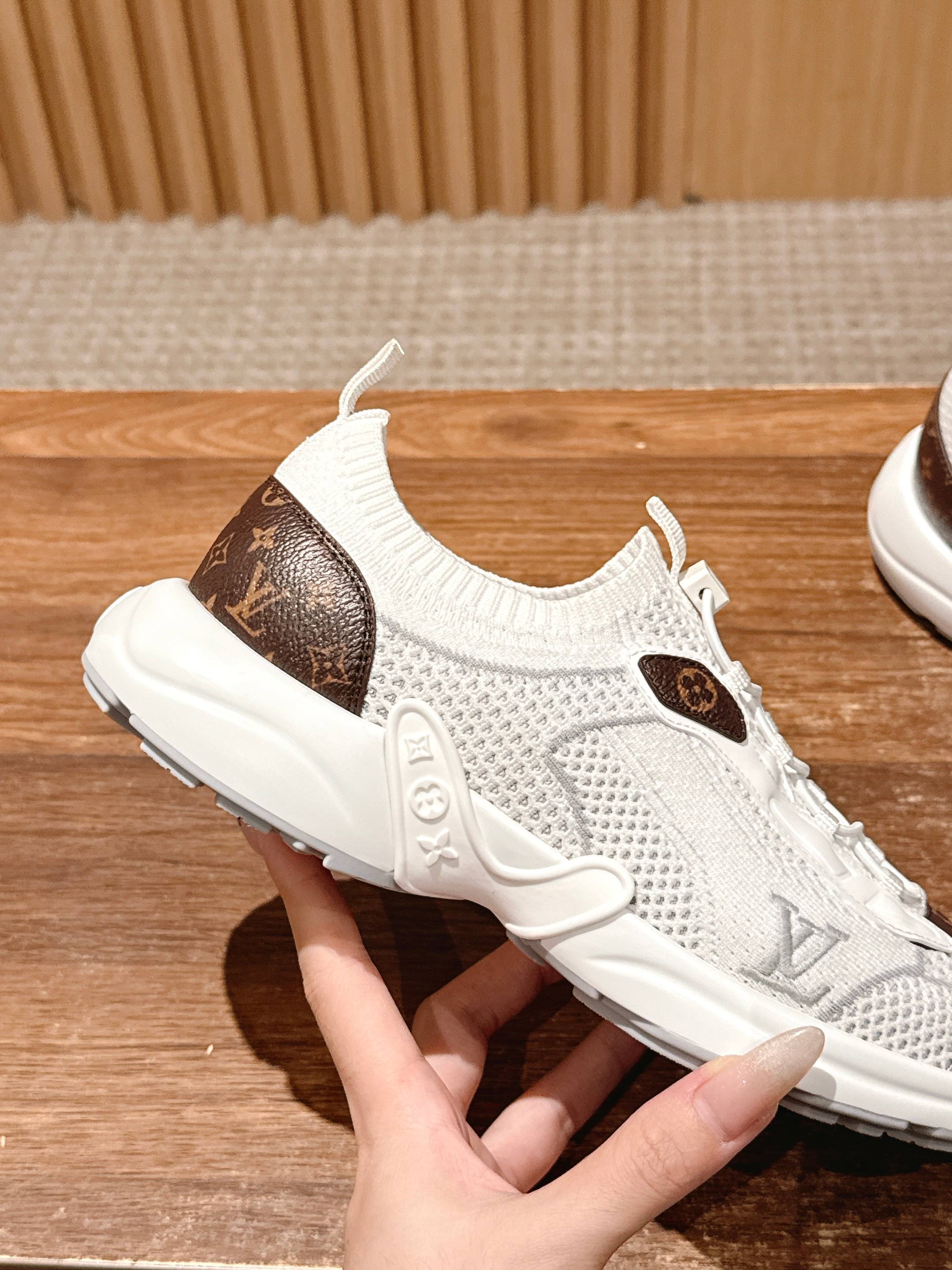 Louis Vuitton unisex white sneakers being held; brown logo patch on mesh upper