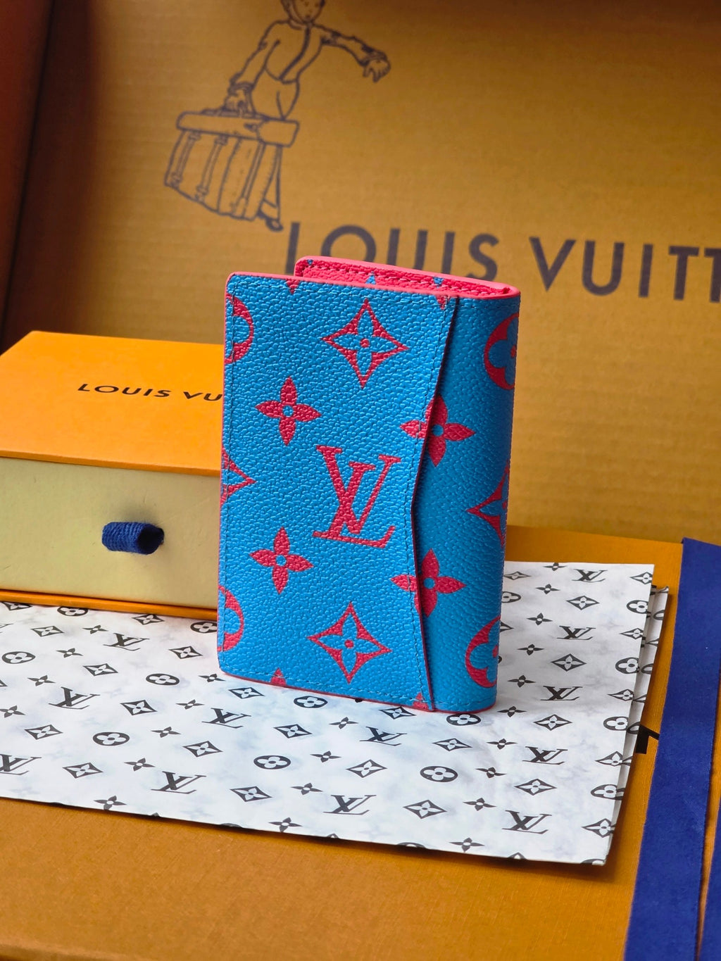 Small bag in bright blue with red monogram-style pattern, angled view
