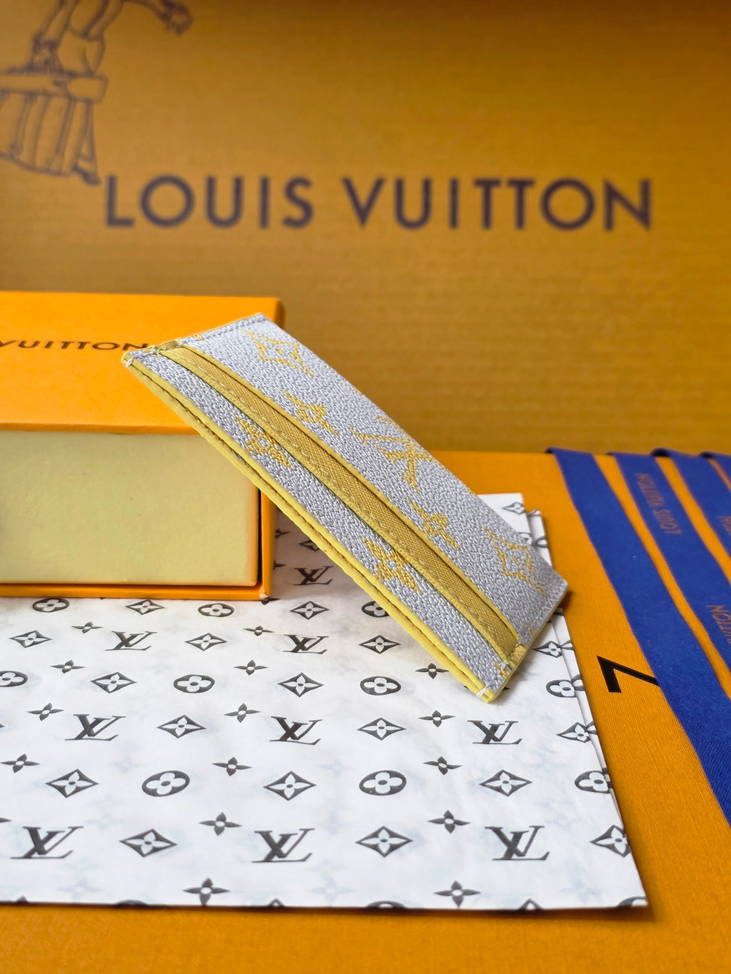 Louis Vuitton small bag with light blue monogram canvas, shown from the side on a box