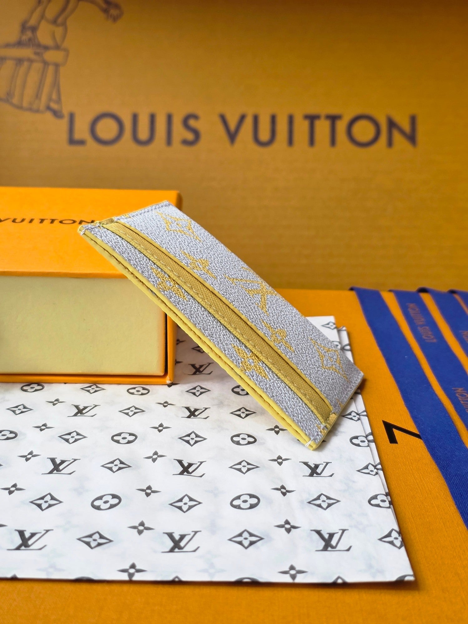 Louis Vuitton small bag with light blue monogram canvas, shown from the side on a box